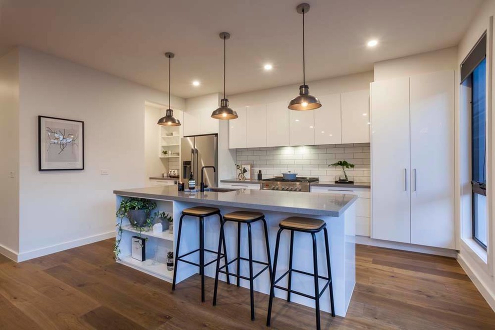 Mid-sized contemporary single-wall open plan kitchen in Melbourne with an undermount sink, flat-panel cabinets, white cabinets, concrete benchtops, white splashback, subway tile splashback, stainless steel appliances, light hardwood floors and with island.