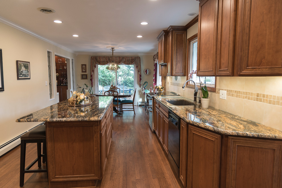 Mid-sized arts and crafts l-shaped eat-in kitchen in Baltimore with an undermount sink, recessed-panel cabinets, medium wood cabinets, granite benchtops, beige splashback, ceramic splashback, black appliances, medium hardwood floors, with island and brown floor.