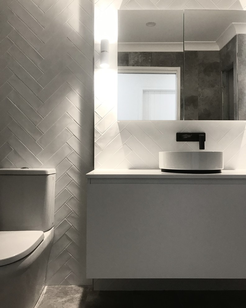 Photo of a mid-sized contemporary 3/4 bathroom in Other with flat-panel cabinets, white cabinets, an alcove shower, a one-piece toilet, white tile, ceramic tile, white walls, porcelain floors, a vessel sink, solid surface benchtops, grey floor and a hinged shower door.