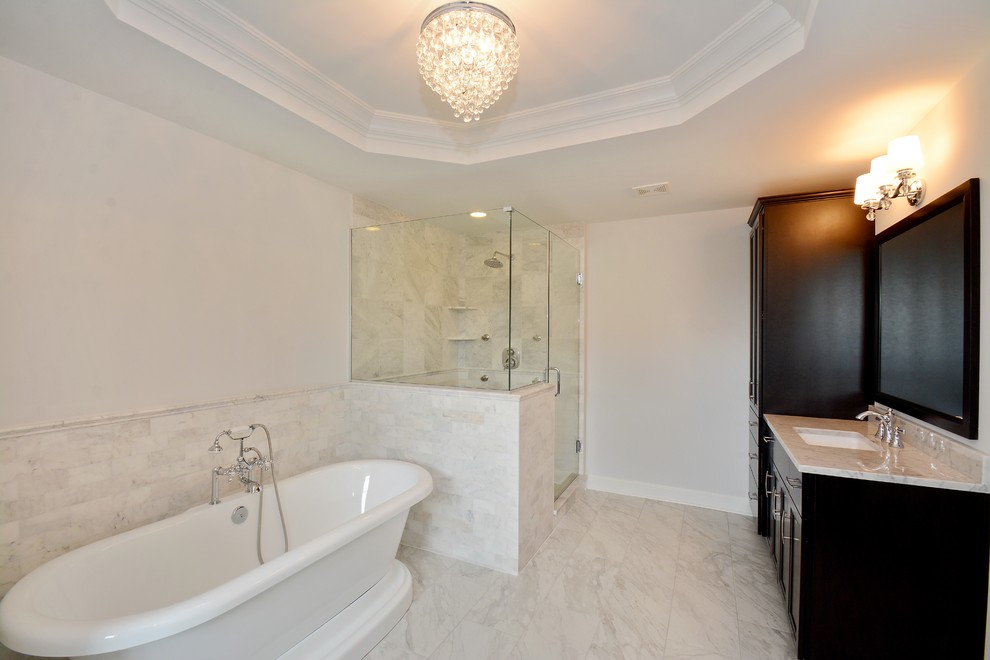 This is an example of a large traditional master bathroom in Chicago with recessed-panel cabinets, dark wood cabinets, a freestanding tub, a corner shower, white tile, white walls, an undermount sink and a hinged shower door.
