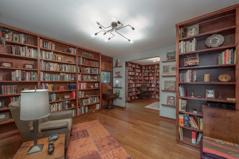 Photo of a mid-sized midcentury home office in Other with a library, white walls, medium hardwood floors, a freestanding desk and brown floor.