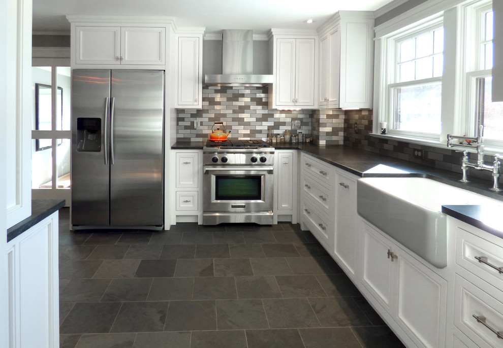 Design ideas for a mid-sized transitional l-shaped kitchen in Boston with a farmhouse sink, recessed-panel cabinets, white cabinets, granite benchtops, metallic splashback, metal splashback, stainless steel appliances, slate floors and a peninsula.