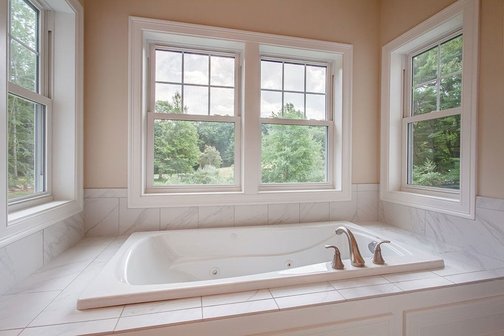 Large transitional master marble floor and white floor drop-in bathtub photo with shaker cabinets, black cabinets, beige walls, an undermount sink and marble countertops