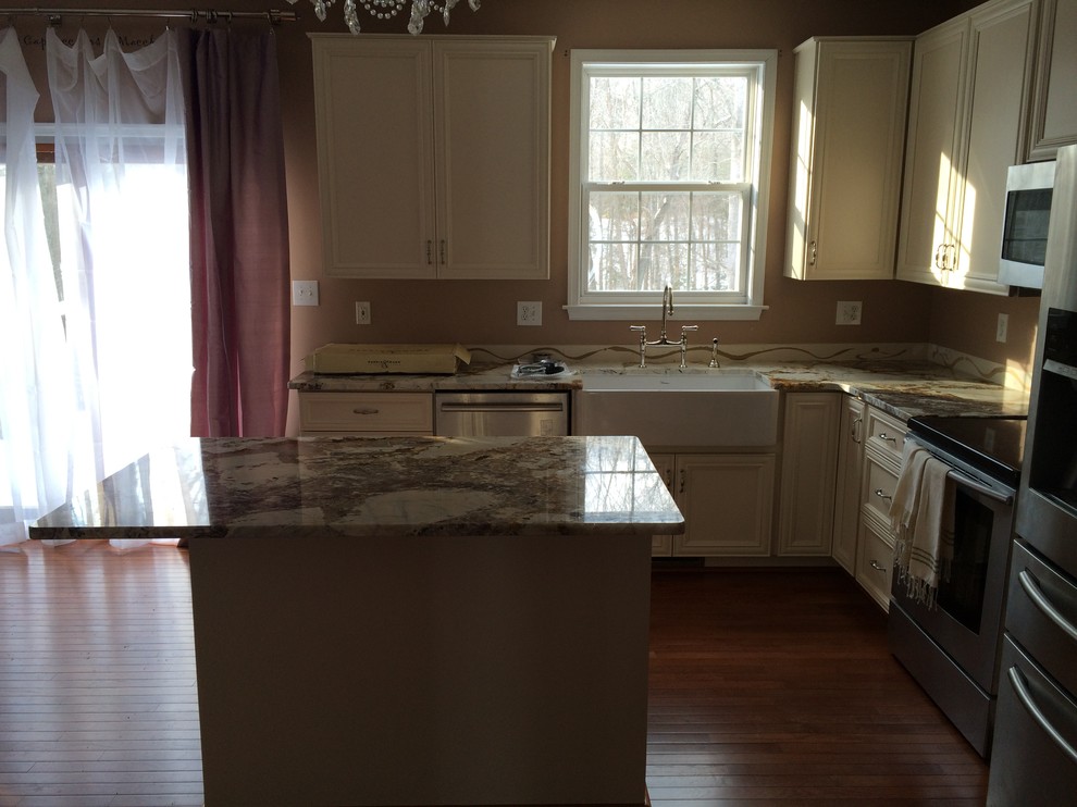 Mid-sized transitional u-shaped open plan kitchen in DC Metro with a farmhouse sink, recessed-panel cabinets, white cabinets, granite benchtops, stainless steel appliances, medium hardwood floors and with island.