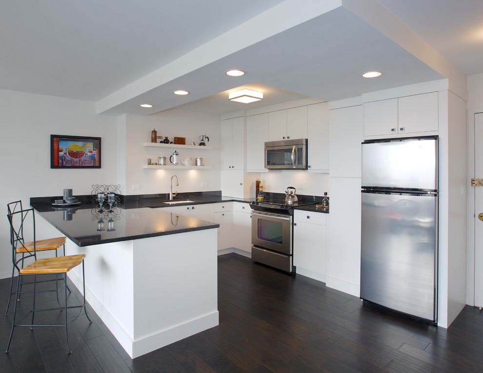 This is an example of a small contemporary l-shaped open plan kitchen in Chicago with a drop-in sink, flat-panel cabinets, white cabinets, stainless steel appliances, dark hardwood floors and no island.