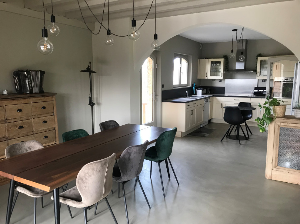 Immagine di una sala da pranzo aperta verso il soggiorno chic di medie dimensioni con pareti beige, pavimento in cemento, pavimento beige, travi a vista e stufa a legna