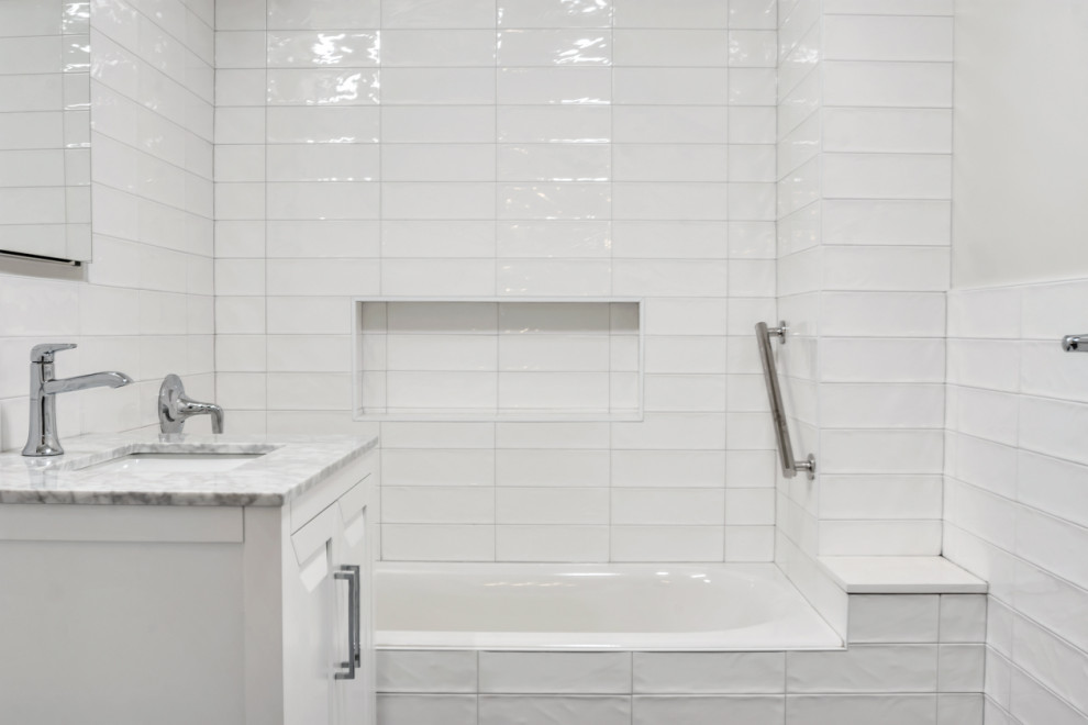 This is an example of a mid-sized modern master bathroom in New York with shaker cabinets, white cabinets, a drop-in tub, a shower/bathtub combo, a two-piece toilet, yellow tile, ceramic tile, white walls, porcelain floors, an integrated sink, marble benchtops, grey floor, a sliding shower screen, grey benchtops, a niche, a single vanity and a freestanding vanity.