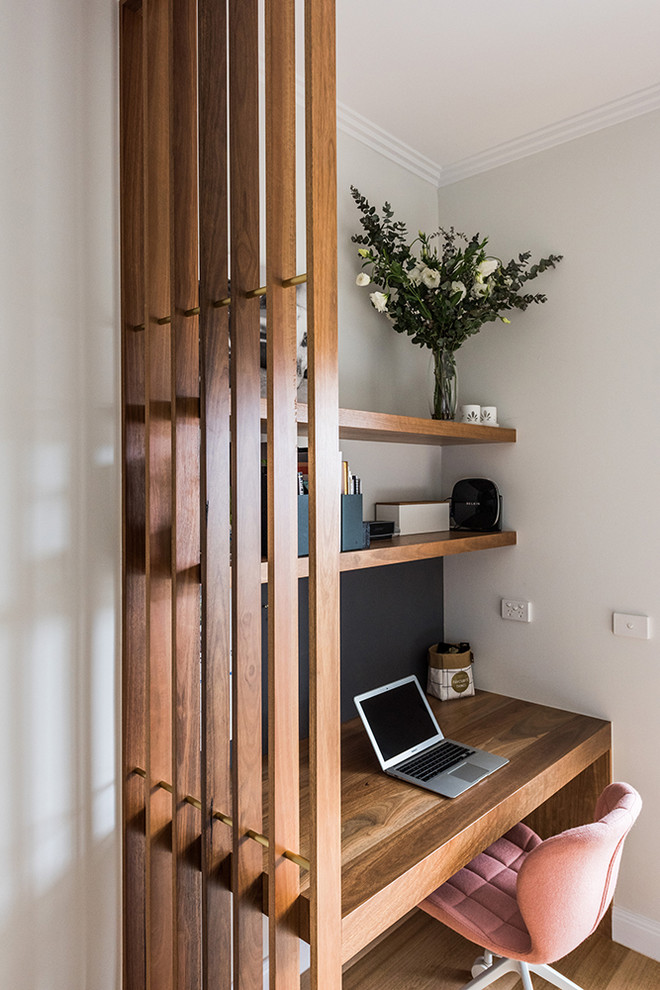 Small transitional study room in Melbourne with white walls, medium hardwood floors, no fireplace, a built-in desk and brown floor.