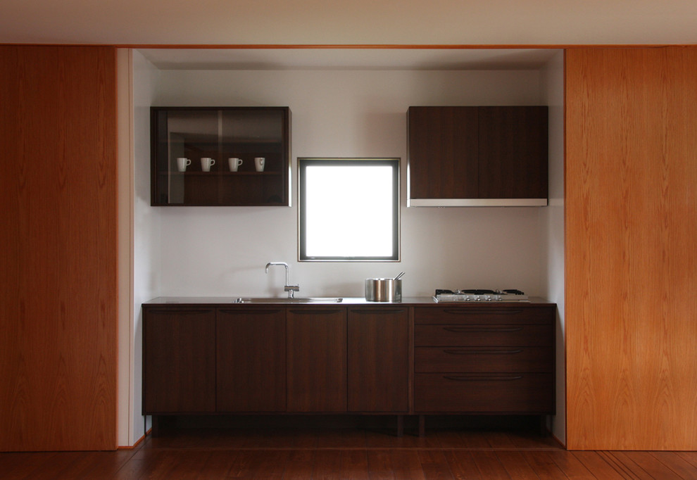 Photo of a small modern single-wall open plan kitchen in Other with an integrated sink, brown cabinets, stainless steel benchtops, brown splashback, stainless steel appliances, medium hardwood floors and brown floor.