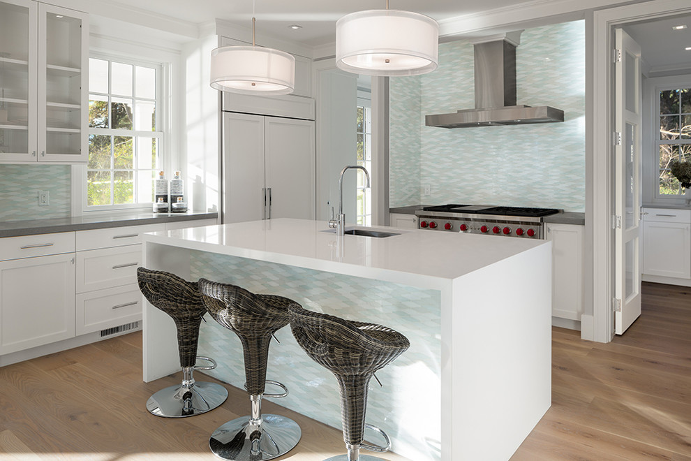 Photo of a mid-sized beach style u-shaped eat-in kitchen in Boston with an undermount sink, shaker cabinets, white cabinets, quartz benchtops, multi-coloured splashback, glass tile splashback, panelled appliances, light hardwood floors and with island.