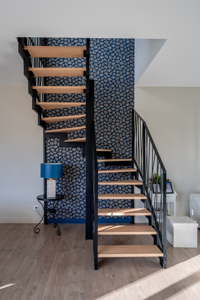 На фото: большая изогнутая лестница в стиле фьюжн с деревянными ступенями, металлическими перилами и обоями на стенах без подступенок