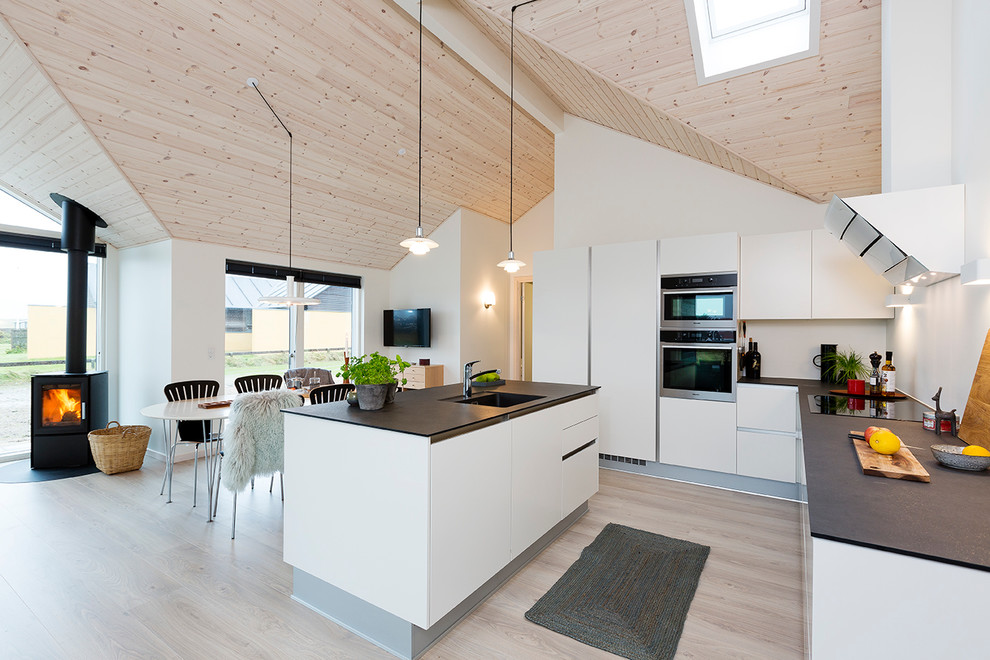 This is an example of a mid-sized scandinavian galley eat-in kitchen in Aarhus with a drop-in sink, flat-panel cabinets, white cabinets, granite benchtops, white splashback, glass sheet splashback, stainless steel appliances, light hardwood floors and with island.