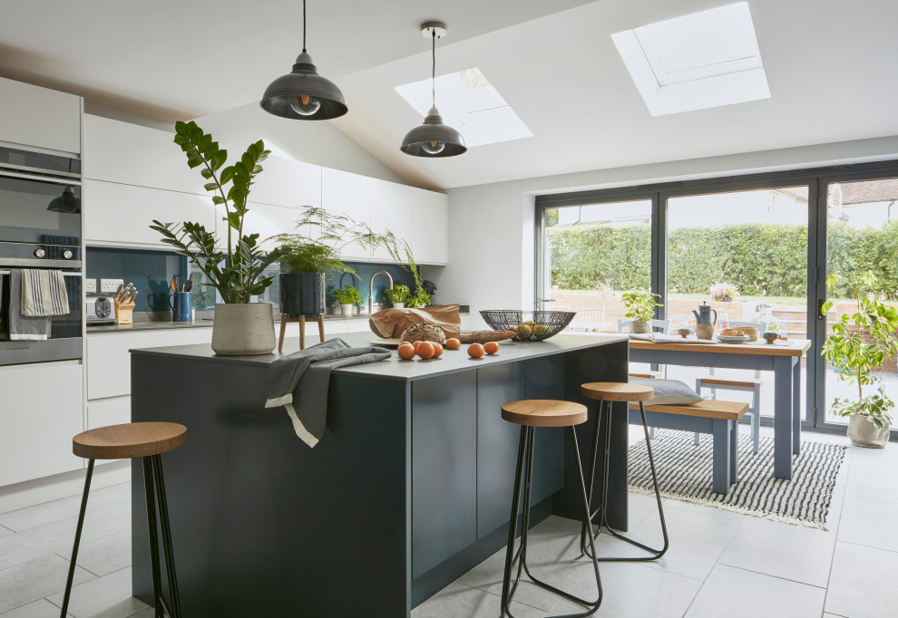 This is an example of a large modern eat-in kitchen in London with blue cabinets, blue splashback, glass sheet splashback, panelled appliances and with island.