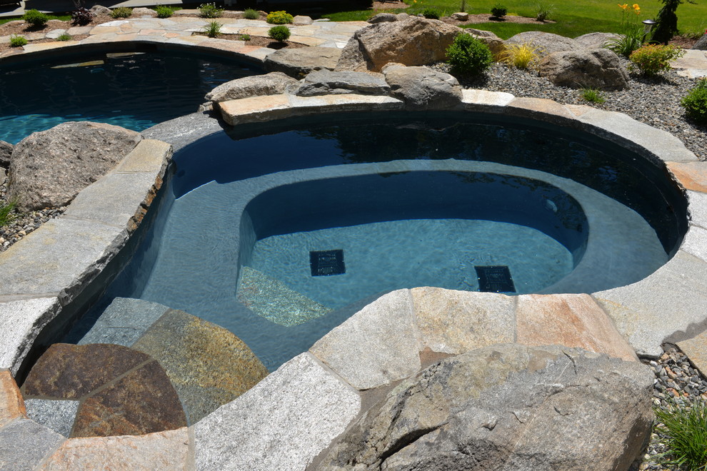 This is an example of a mid-sized tropical backyard custom-shaped natural pool in New York with a hot tub and natural stone pavers.