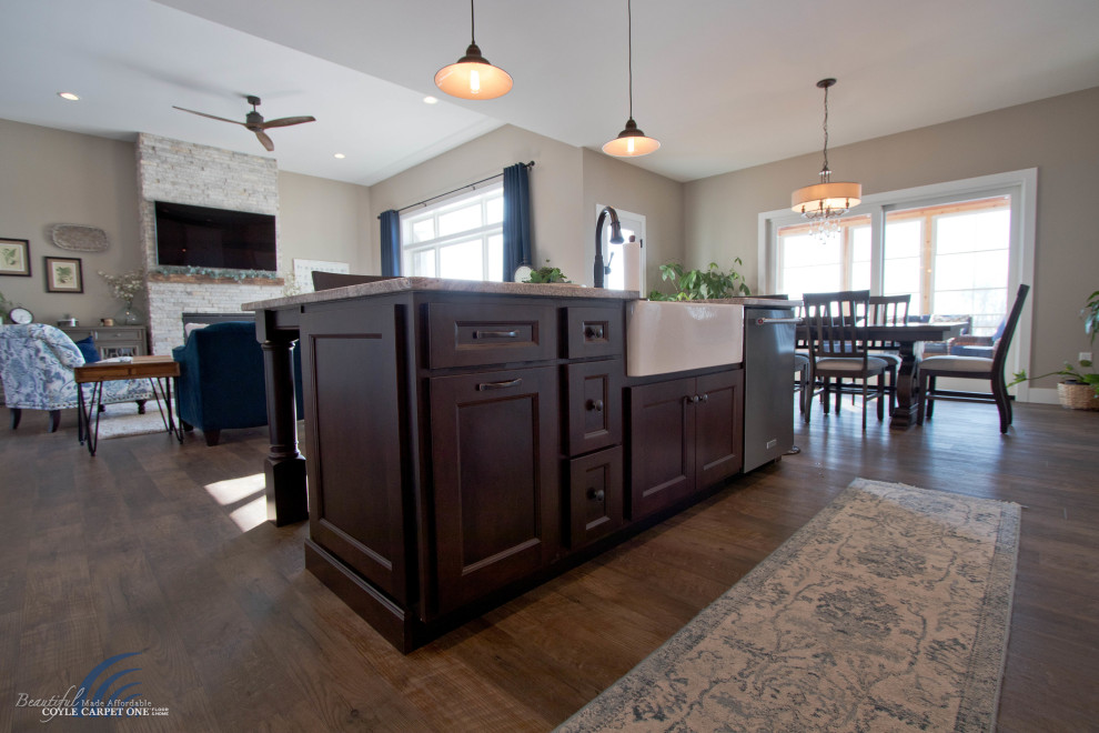 This is an example of a large country l-shaped open plan kitchen in Other with shaker cabinets, white cabinets, granite benchtops, brown splashback, subway tile splashback, stainless steel appliances, vinyl floors, with island, brown floor, a farmhouse sink and grey benchtop.