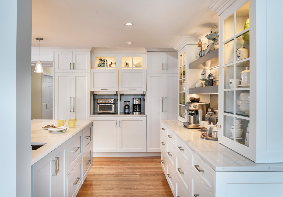 This is an example of a modern u-shaped kitchen in Boston with a submerged sink, flat-panel cabinets, white cabinets, engineered stone countertops, white splashback, stainless steel appliances, light hardwood flooring, an island and white worktops.