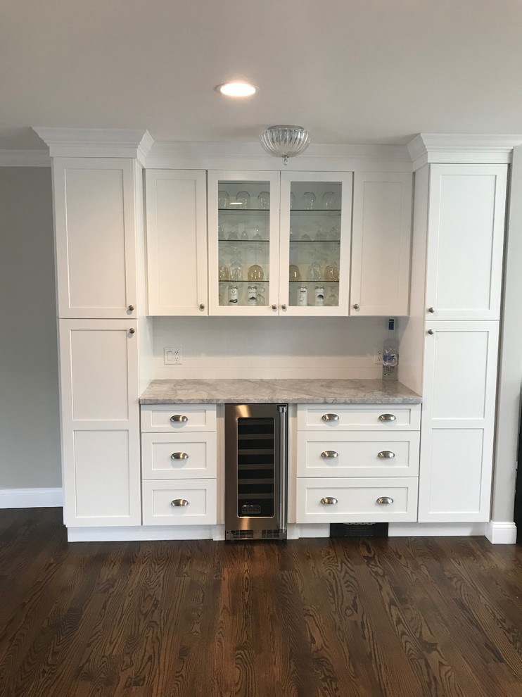 Example of a mid-sized transitional u-shaped dark wood floor and brown floor eat-in kitchen design in New York with a farmhouse sink, recessed-panel cabinets, white cabinets, wood countertops, white backsplash, limestone backsplash, stainless steel appliances, an island and gray countertops