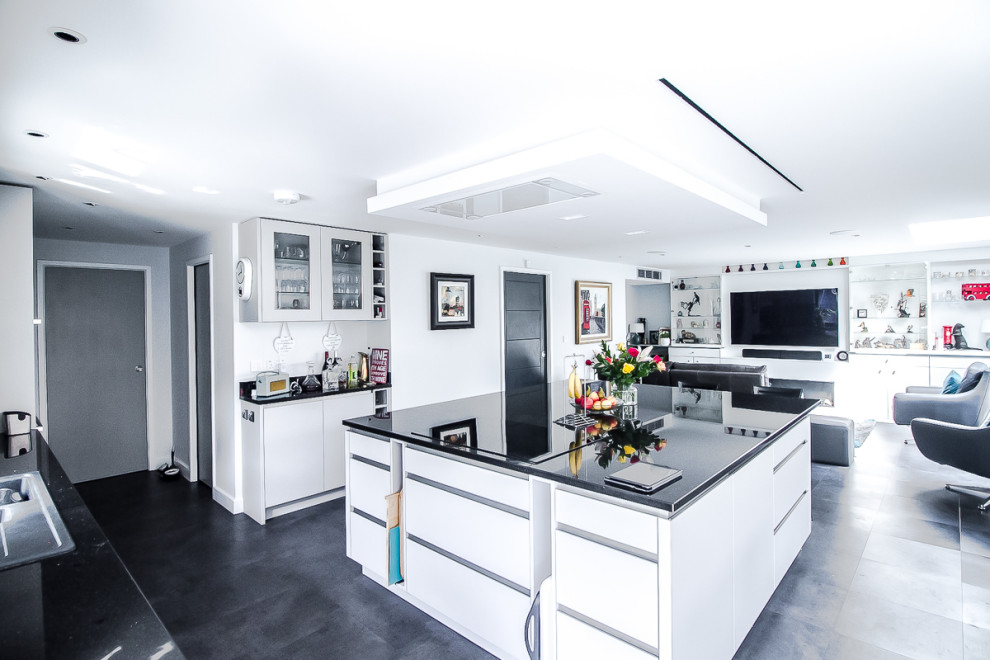 Inspiration for a large modern l-shaped open plan kitchen in London with an integrated sink, flat-panel cabinets, white cabinets, granite worktops, green splashback, glass sheet splashback, integrated appliances, lino flooring, an island, black floors and black worktops.