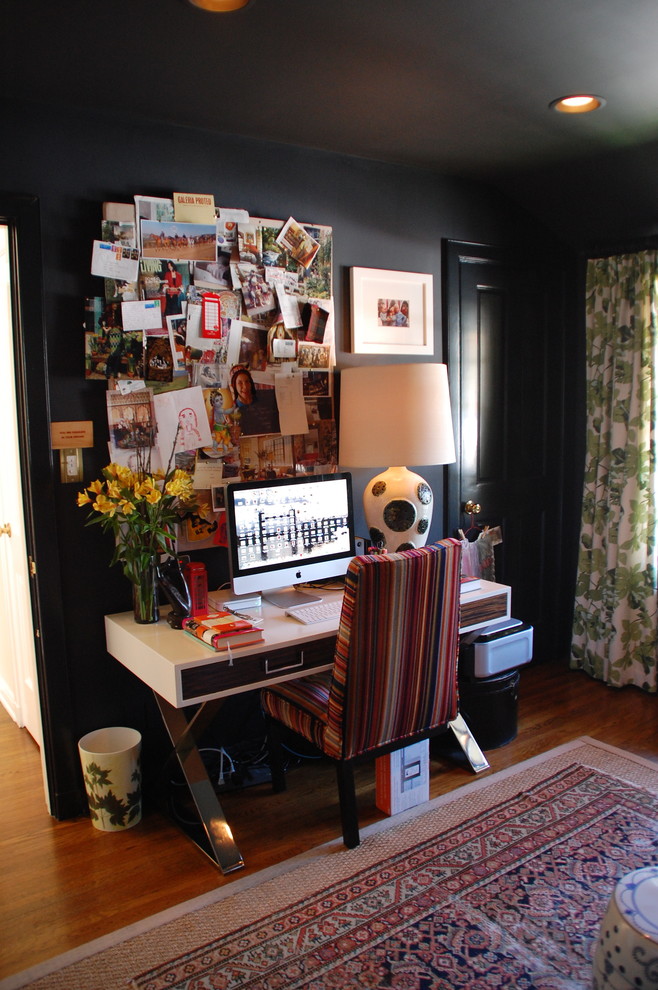 This is an example of an eclectic home office in Los Angeles with black walls, dark hardwood floors, a freestanding desk and brown floor.