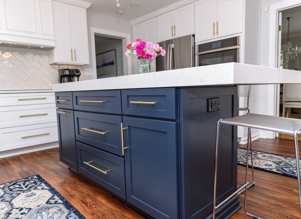 Eat-in kitchen - mid-sized transitional galley brown floor and medium tone wood floor eat-in kitchen idea in Baltimore with shaker cabinets, white cabinets, quartz countertops, white backsplash, subway tile backsplash, stainless steel appliances, an island, white countertops and an undermount sink