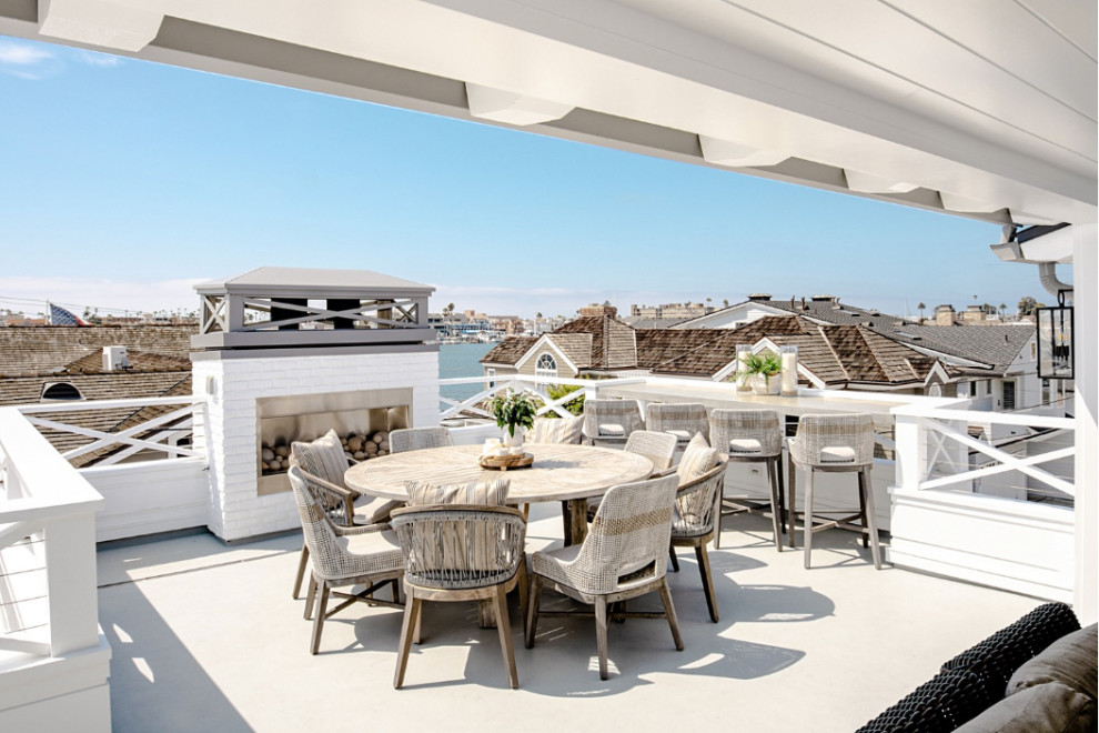 This is an example of a large beach style rooftop deck in Orange County with with fireplace and a roof extension.