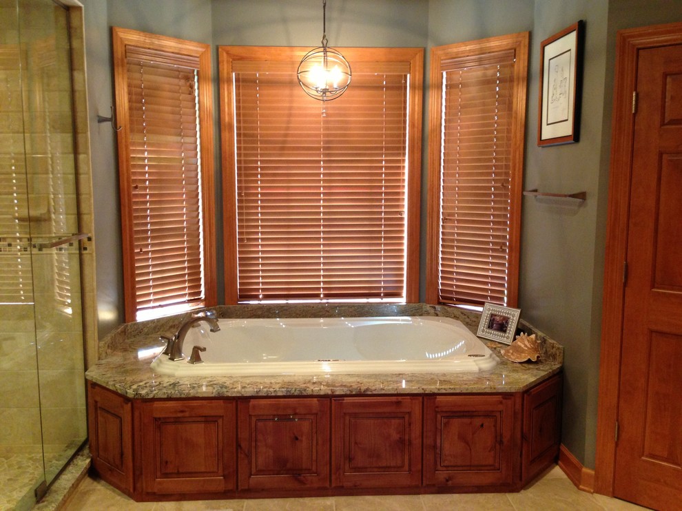 Example of a mountain style drop-in bathtub design in St Louis with raised-panel cabinets, distressed cabinets and granite countertops