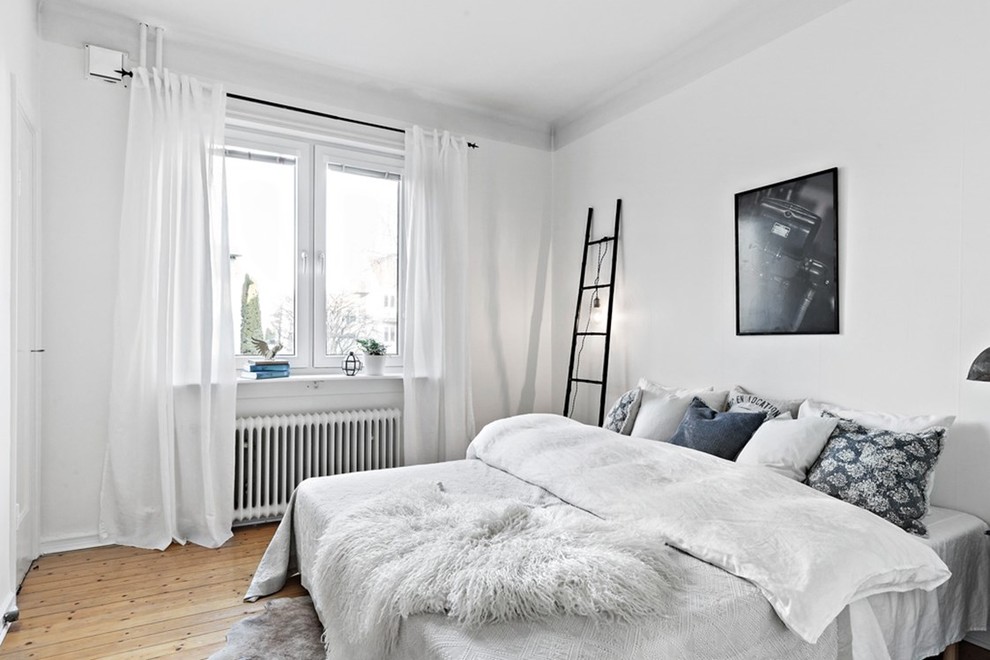 Scandinavian bedroom in Gothenburg with white walls, medium hardwood floors and brown floor.