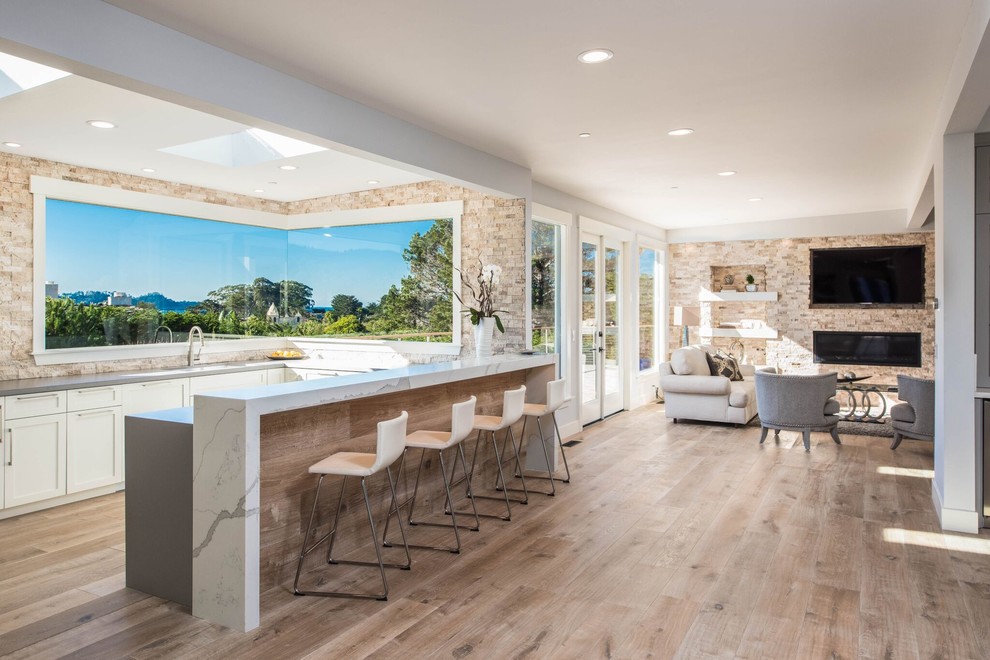 Open concept kitchen - large transitional u-shaped light wood floor open concept kitchen idea in Orange County with shaker cabinets, white cabinets, stone tile backsplash, no island, an undermount sink and gray countertops