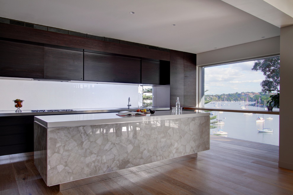 Photo of a large modern galley kitchen in Sydney with an undermount sink, flat-panel cabinets, dark wood cabinets, quartz benchtops, glass sheet splashback, stainless steel appliances, medium hardwood floors and with island.