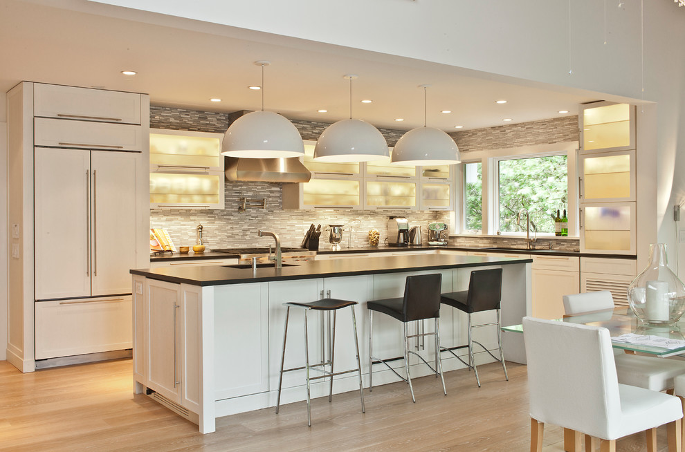 Photo of a large contemporary l-shaped eat-in kitchen in New York with an undermount sink, glass-front cabinets, white cabinets, grey splashback, matchstick tile splashback, stainless steel appliances, light hardwood floors and with island.