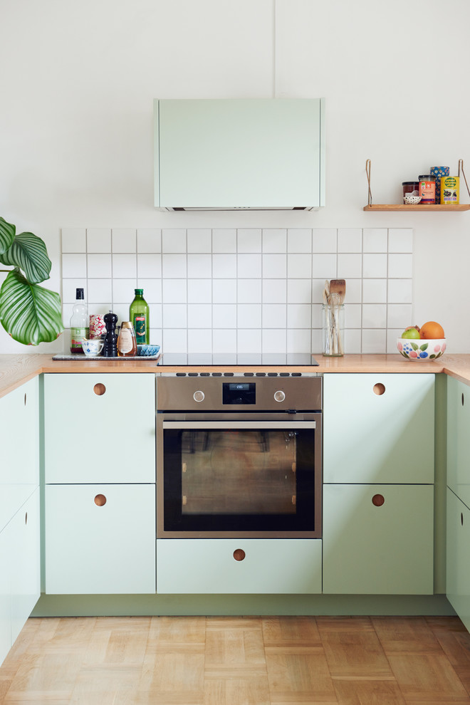 Scandinavian u-shaped eat-in kitchen in Berlin with an integrated sink, flat-panel cabinets, green cabinets, wood benchtops and light hardwood floors.