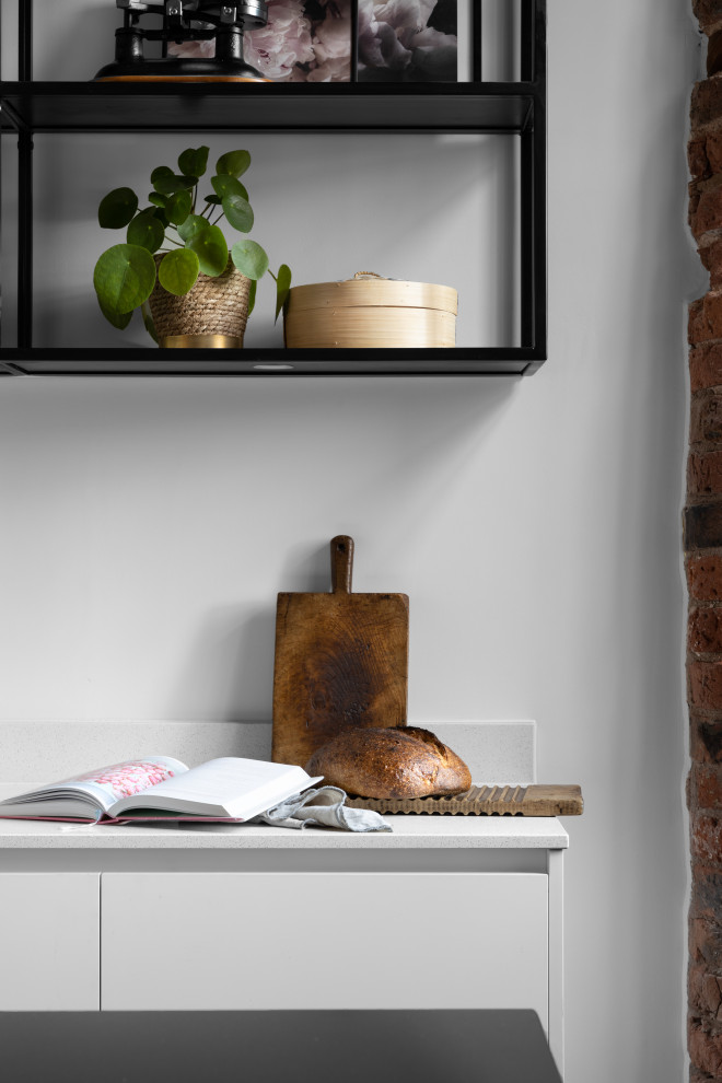 Design ideas for a large rustic l-shaped open plan kitchen in Manchester with an integrated sink, flat-panel cabinets, white cabinets, engineered stone countertops, white splashback, stone slab splashback, stainless steel appliances, porcelain flooring, an island, grey floors, black worktops, exposed beams and feature lighting.