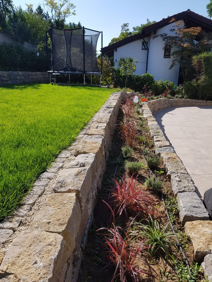 Inspiration för mellanstora medelhavsstil formella trädgårdar i delvis sol i slänt på våren, med en stödmur och naturstensplattor