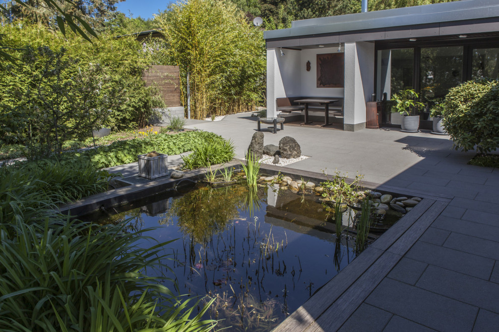 Medium sized traditional garden with a pond and concrete paving.