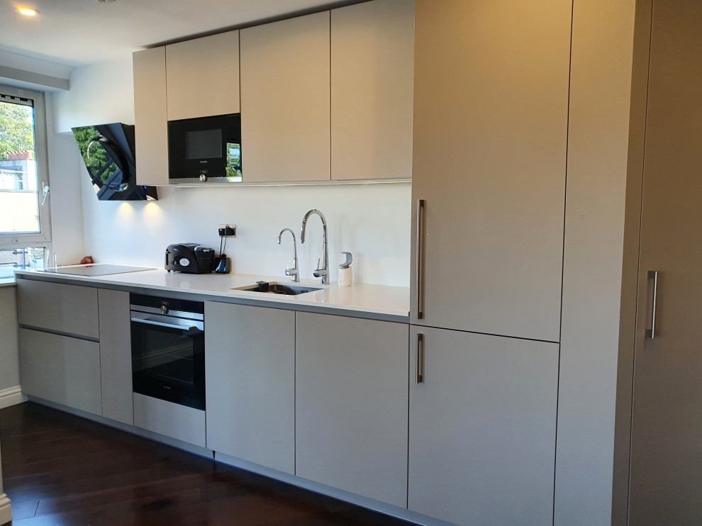 Photo of a medium sized contemporary single-wall open plan kitchen in London with a single-bowl sink, flat-panel cabinets, beige cabinets, quartz worktops, white splashback, dark hardwood flooring, brown floors and white worktops.