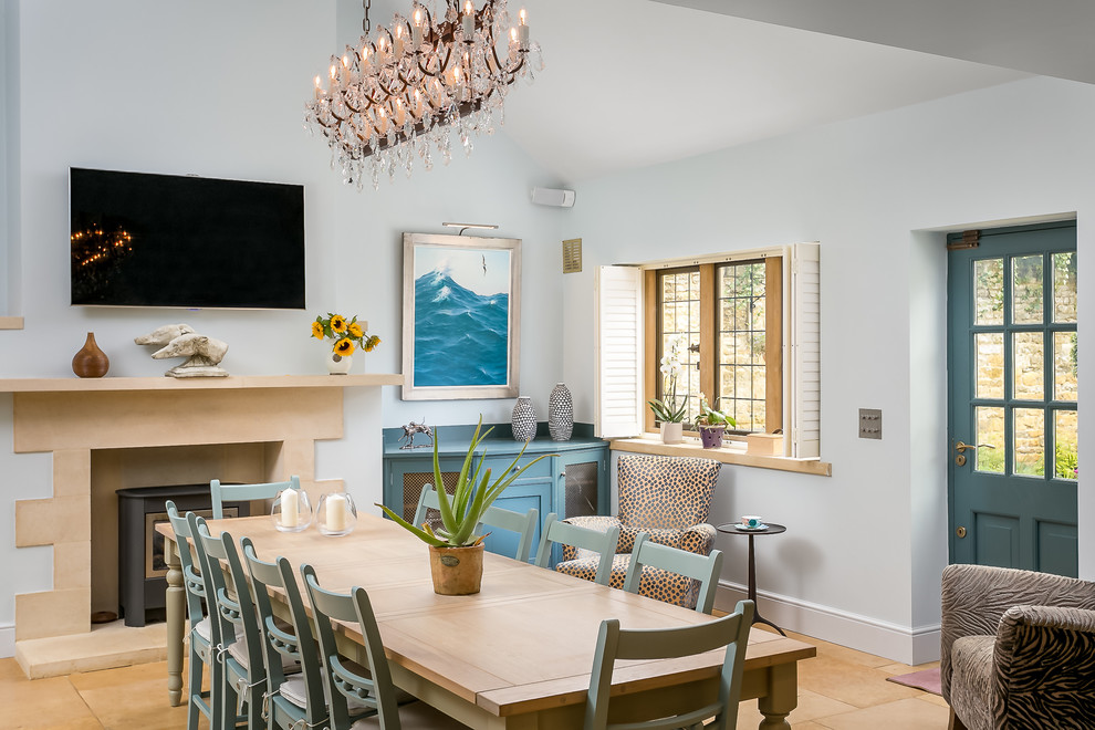 Photo of a large transitional kitchen/dining combo in Gloucestershire with blue walls, limestone floors, a wood stove, a stone fireplace surround and brown floor.