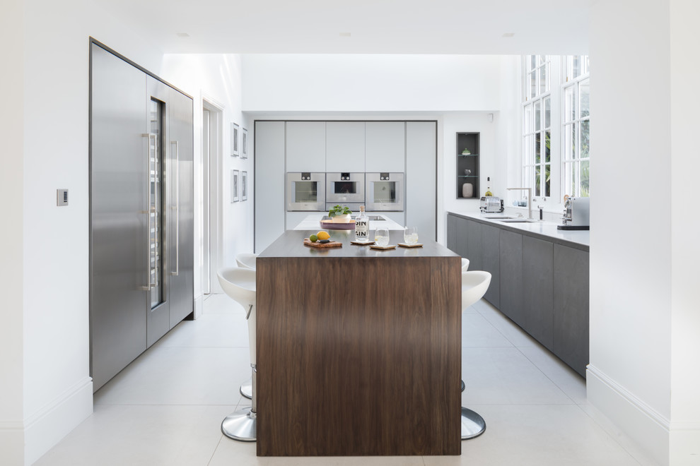 Inspiration for a large contemporary u-shaped kitchen in London with a double-bowl sink, flat-panel cabinets, stainless steel cabinets, stainless steel appliances, with island and grey floor.
