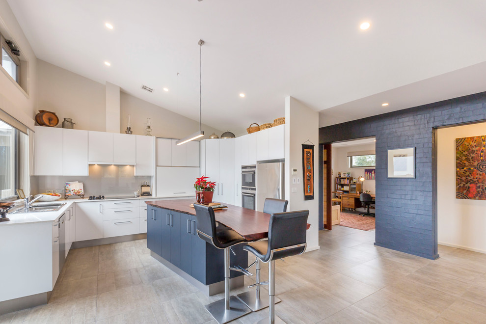 This is an example of a contemporary u-shaped eat-in kitchen in Canberra - Queanbeyan with a drop-in sink, flat-panel cabinets, white cabinets, grey splashback, glass sheet splashback, stainless steel appliances, with island, grey floor and white benchtop.