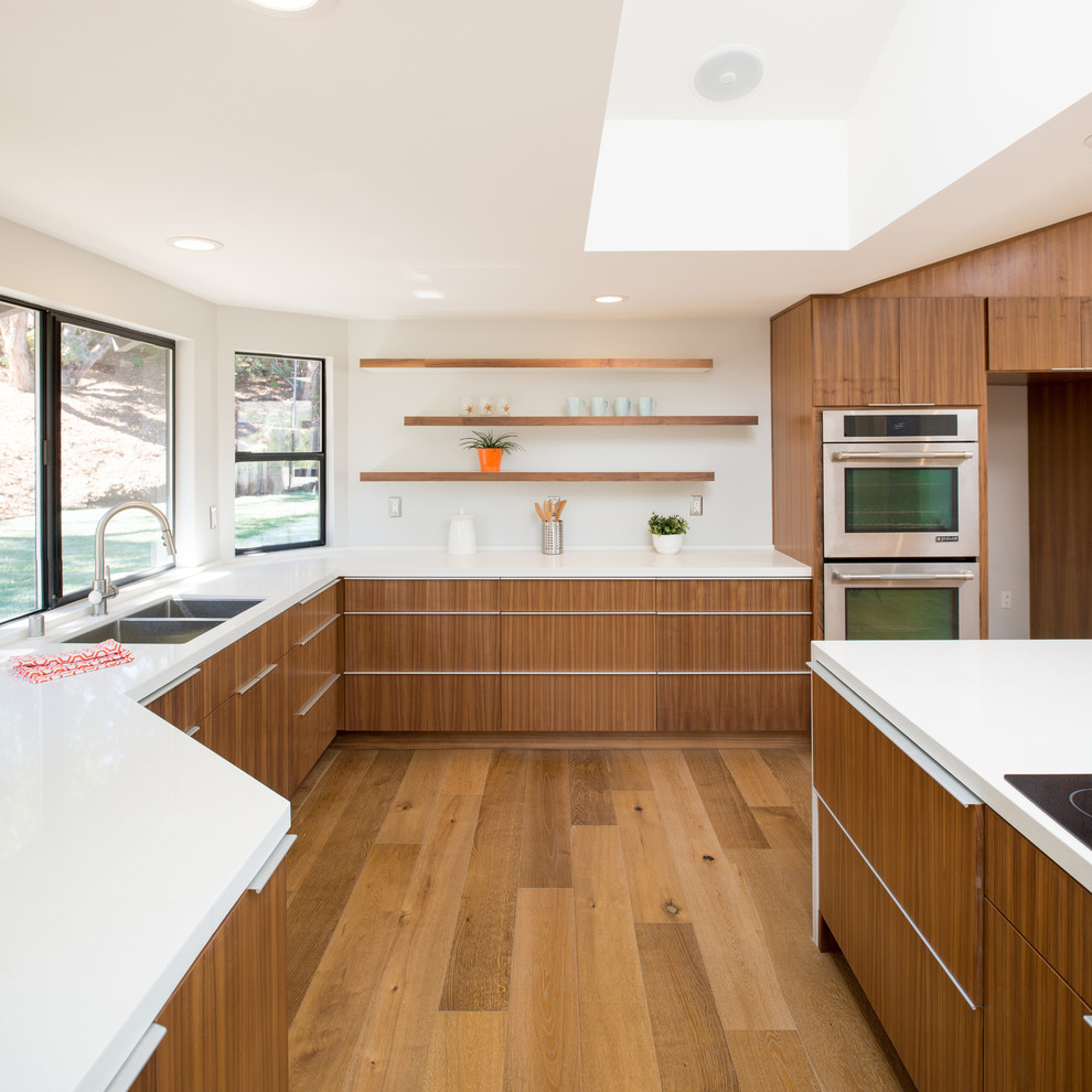 Photo of a large midcentury u-shaped open plan kitchen in San Diego with medium wood cabinets, white splashback, stainless steel appliances, light hardwood floors and with island.