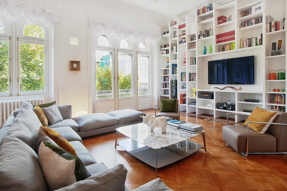 Photo of a contemporary enclosed living room in Milan with a library, white walls, medium hardwood floors and a built-in media wall.