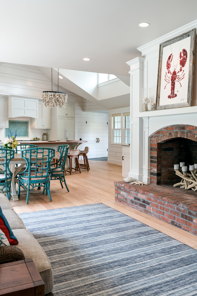 This is an example of a beach style open concept living room in Boston with white walls, light hardwood floors, a standard fireplace, a brick fireplace surround and beige floor.