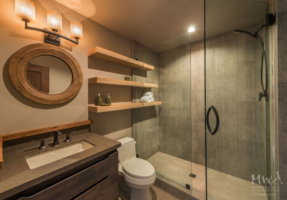 Mid-sized mountain style gray tile and porcelain tile porcelain tile and beige floor double shower photo with flat-panel cabinets, gray cabinets, a one-piece toilet, beige walls, an undermount sink, marble countertops, a hinged shower door and gray countertops