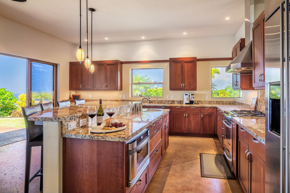 Photo of a large arts and crafts l-shaped eat-in kitchen in Hawaii with a double-bowl sink, raised-panel cabinets, medium wood cabinets, granite benchtops, stone slab splashback, stainless steel appliances, concrete floors and with island.