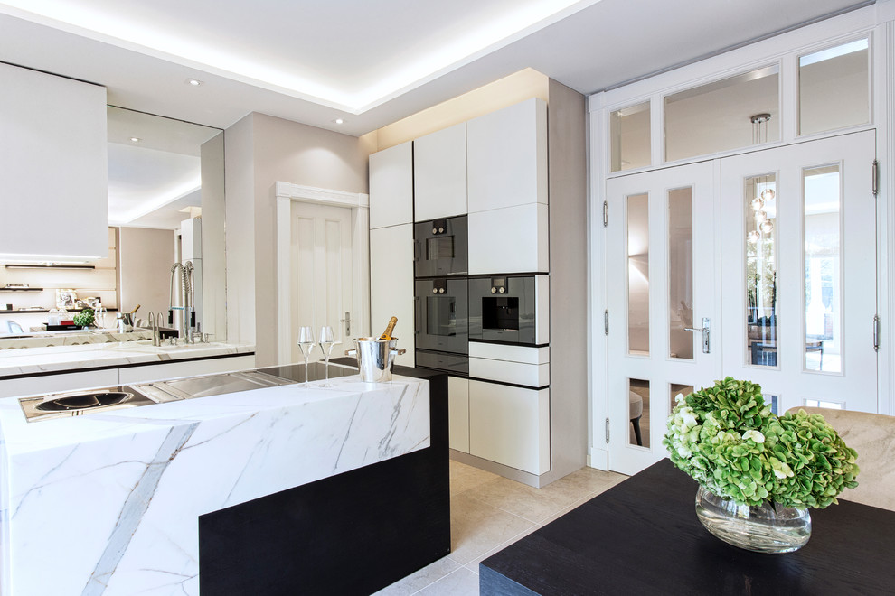 Photo of a large transitional separate kitchen in Hamburg with a drop-in sink, flat-panel cabinets, white cabinets, marble benchtops, black appliances, travertine floors and with island.