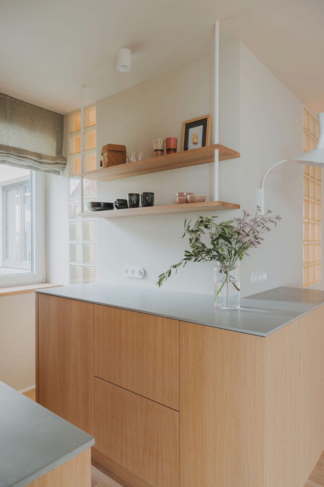 Küche in L-Form mit integriertem Waschbecken, flächenbündigen Schrankfronten, hellen Holzschränken, Mineralwerkstoff-Arbeitsplatte, Küchenrückwand in Weiß, Rückwand aus Mosaikfliesen, schwarzen Elektrogeräten, hellem Holzboden, braunem Boden und grauer Arbeitsplatte in Munich