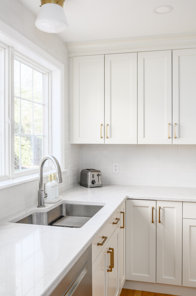 Large traditional l-shaped eat-in kitchen in Boston with an undermount sink, recessed-panel cabinets, white cabinets, quartzite benchtops, white splashback, ceramic splashback, stainless steel appliances, medium hardwood floors, with island, brown floor and white benchtop.