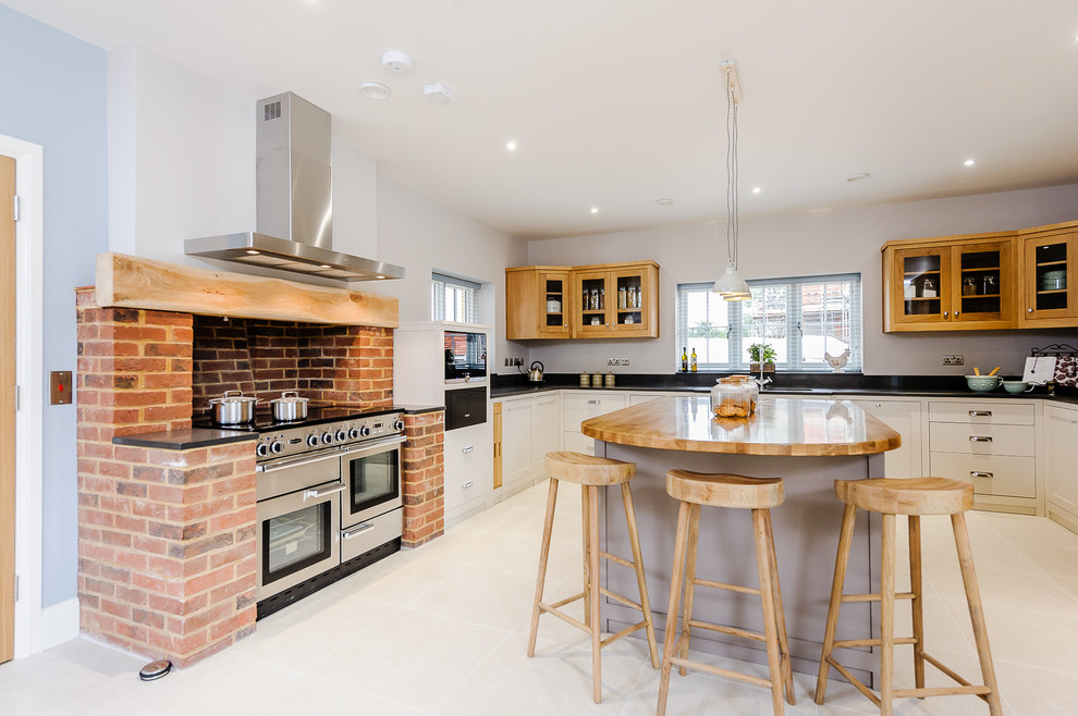 Photo of a large country u-shaped separate kitchen in Essex with an undermount sink, recessed-panel cabinets, beige cabinets, granite benchtops, orange splashback, brick splashback, stainless steel appliances, with island, grey floor and black benchtop.
