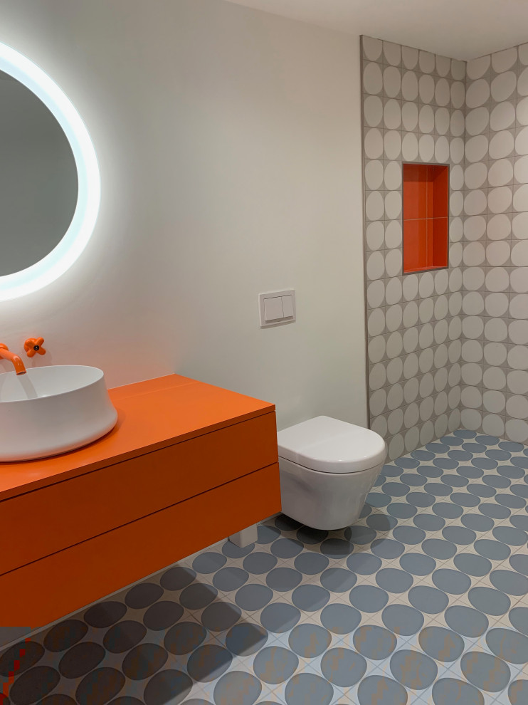 Photo of a mid-sized modern bathroom in Los Angeles with flat-panel cabinets, orange cabinets, a curbless shower, a wall-mount toilet, gray tile, porcelain tile, white walls, porcelain floors, a vessel sink, laminate benchtops, blue floor, a hinged shower door and orange benchtops.