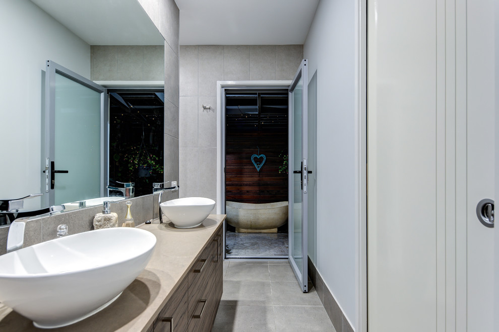 This is an example of a mid-sized contemporary wet room bathroom in Sunshine Coast with dark wood cabinets, a freestanding tub, gray tile, porcelain tile, grey walls, porcelain floors, a vessel sink, engineered quartz benchtops, grey floor, brown benchtops, a one-piece toilet and a hinged shower door.