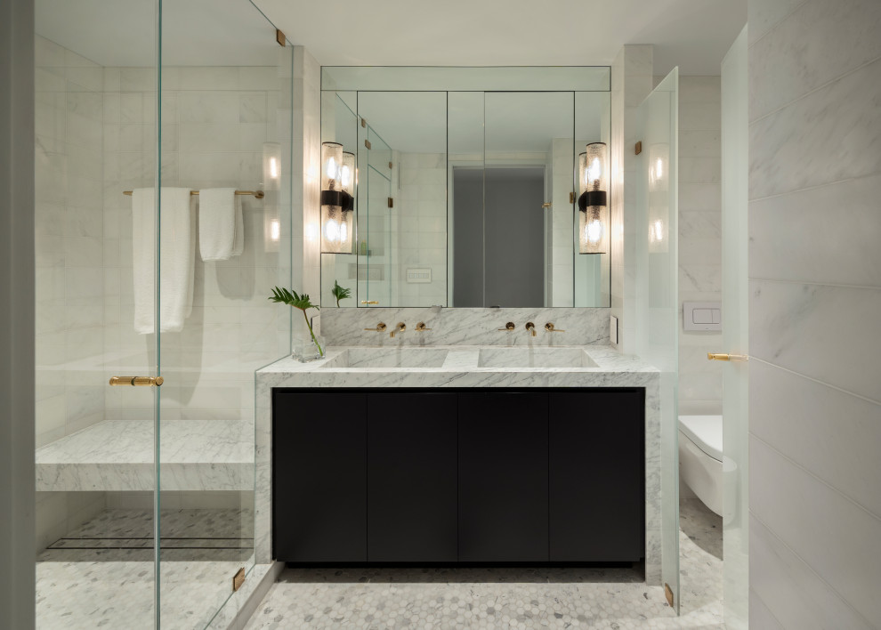 This is an example of a contemporary bathroom in New York with flat-panel cabinets, black cabinets, an alcove shower, a wall mounted toilet, grey tiles, marble flooring, an integrated sink, grey floors, a hinged door, grey worktops, a shower bench, an enclosed toilet, double sinks and a built in vanity unit.